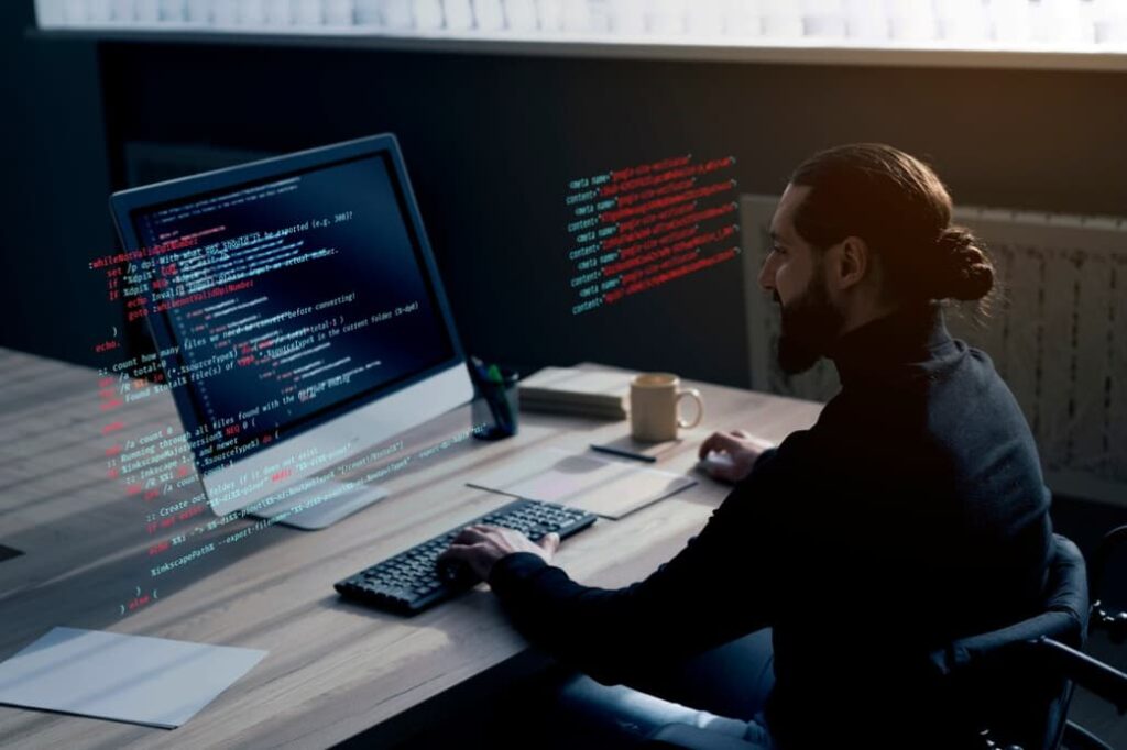 Man coding on a computer in a dimly lit room